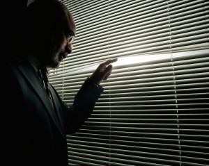 Mature man peeking through window blinds